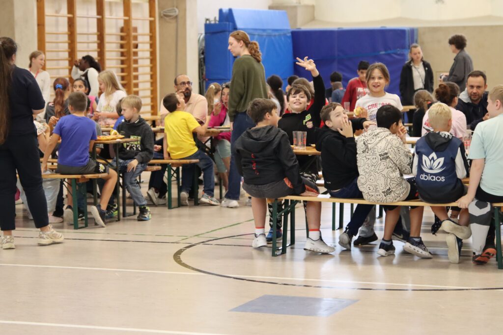Schülerinnen und Schüler essen gemeinsam in einer Turnhalle