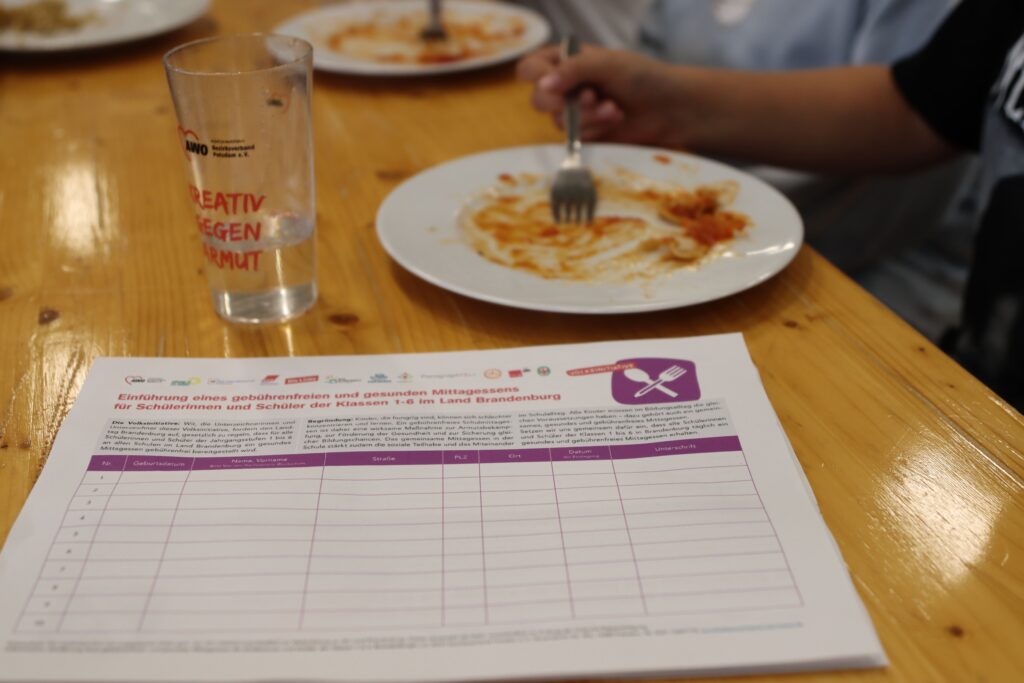 Unterschriftenliste der Volksinitiative auf einem Tisch mit leer gegessenen Tellern